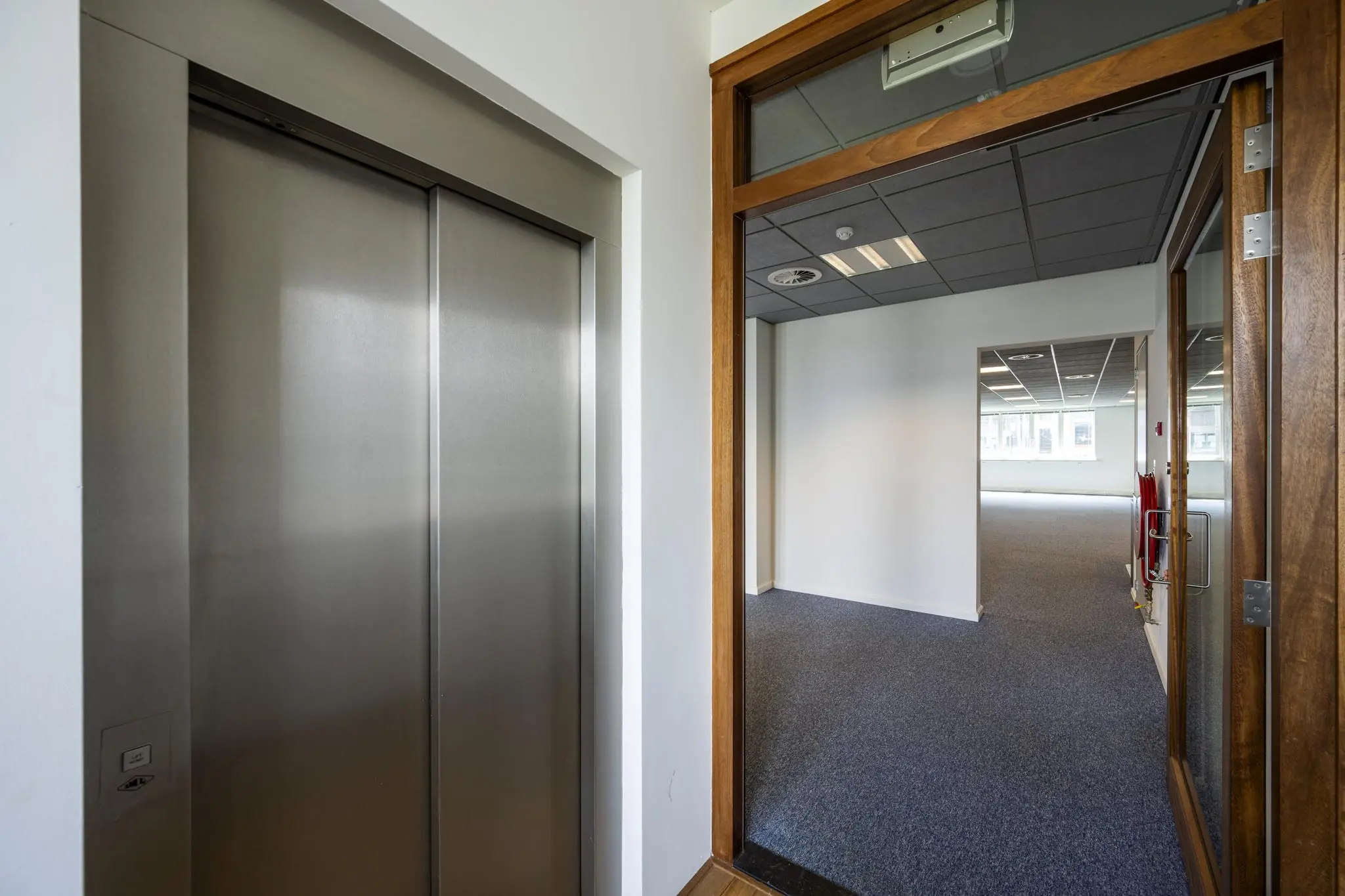 Entree van een modern kantoorpand aan de De Ruijterkade met een gesloten liftdeur en zicht op een lege kantoorruimte.